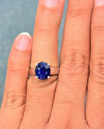 Load image into Gallery viewer, Close-up of a hand wearing a ring with a blue sapphire against a neutral background
